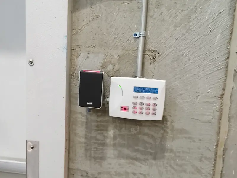 DSC PowerSeries commercial alarm keypad and HID card reader wired in surface EMT conduit beside a warehouse exit door in Mississauga, ON.