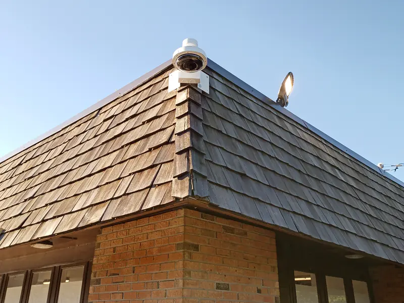 Axis exterior multi-directional camera on a pendant gooseneck mount at the roofline corner of a commercial plaza in Burlington, ON.