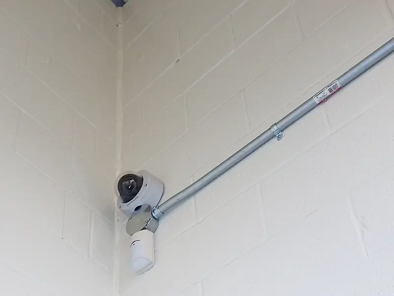 Avigilon dome camera on a block wall corner, fed by surface EMT conduit, in an underground garage.