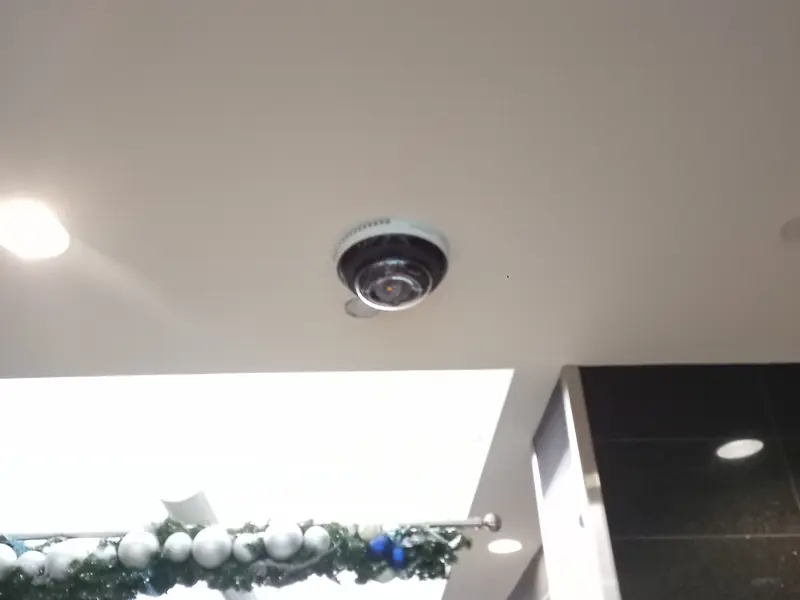 Axis indoor dome camera mounted in a finished ceiling beside recessed lighting in an office lobby.