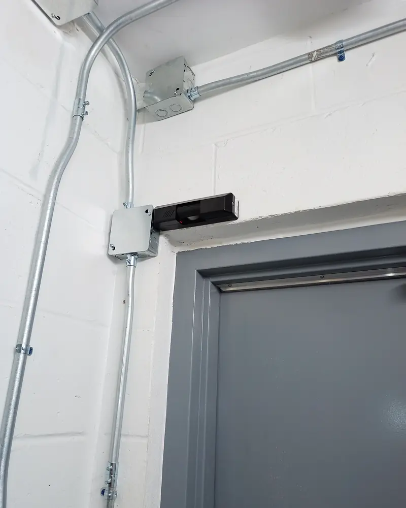 EMT conduit and junction box above a steel door frame feeding an electric strike, door position switch and REX sensor in Brampton, ON.