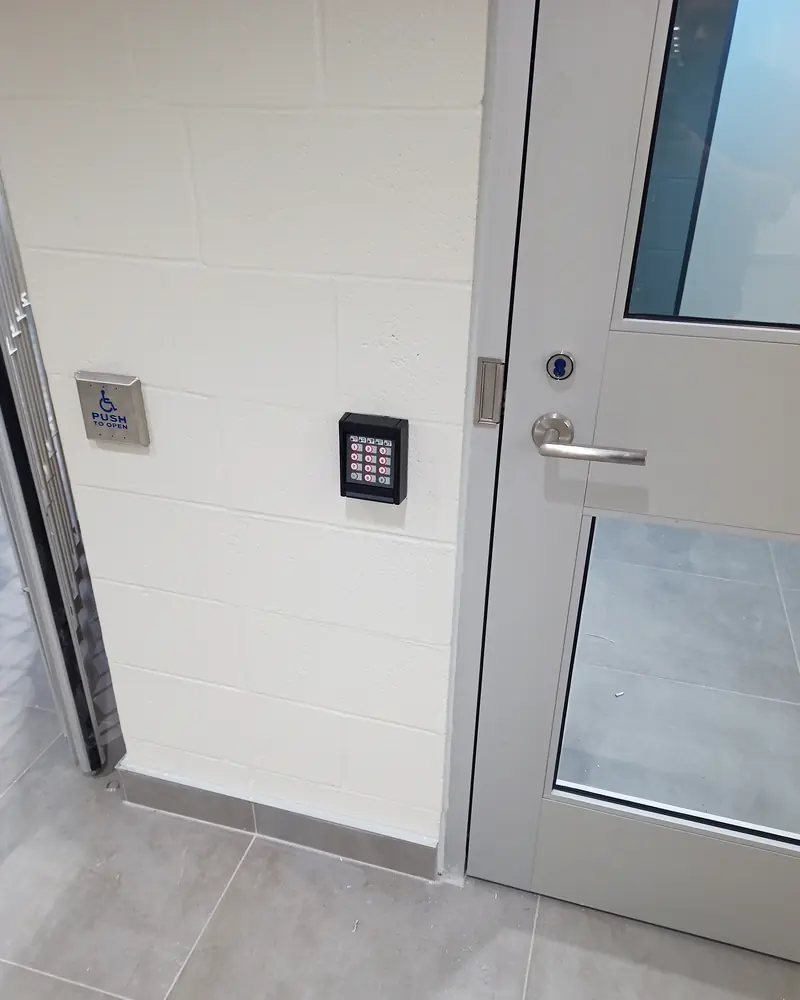 HID keypad card reader and accessible automatic door operator push button mounted beside a glazed commercial office entrance in Toronto, ON.