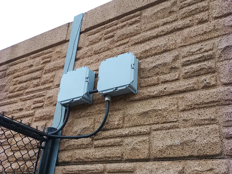 Weatherproof PVC junction boxes and liquid-tight flexible conduit transitioning underground yard fibre and gate power at a fence line in Bolton, ON.