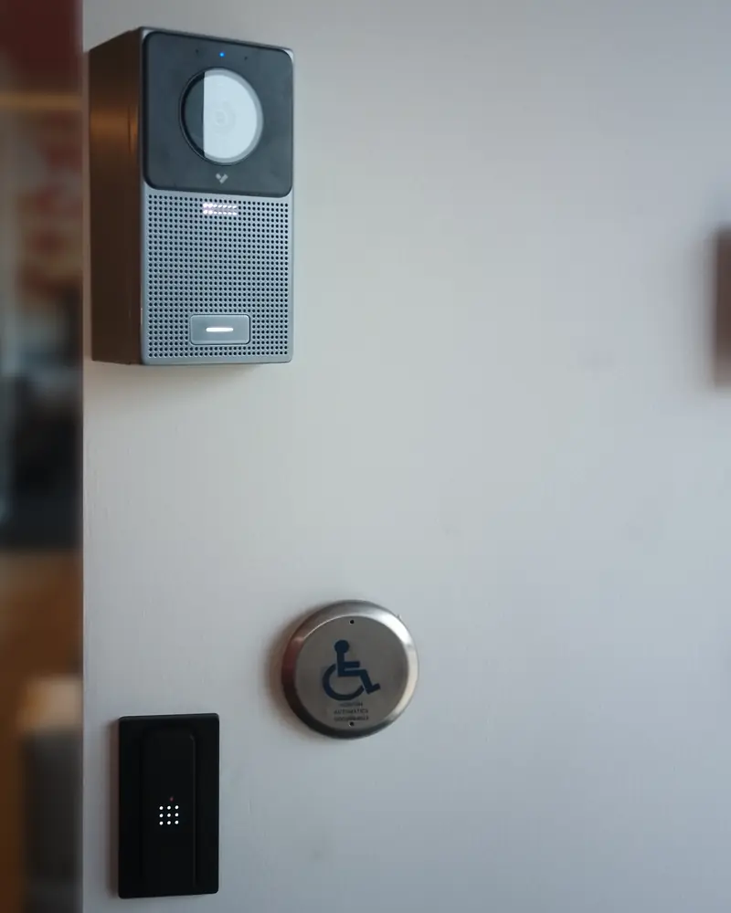 Aiphone IP video intercom station mounted on a vestibule wall above an accessible door button and HID card reader in North York, ON.