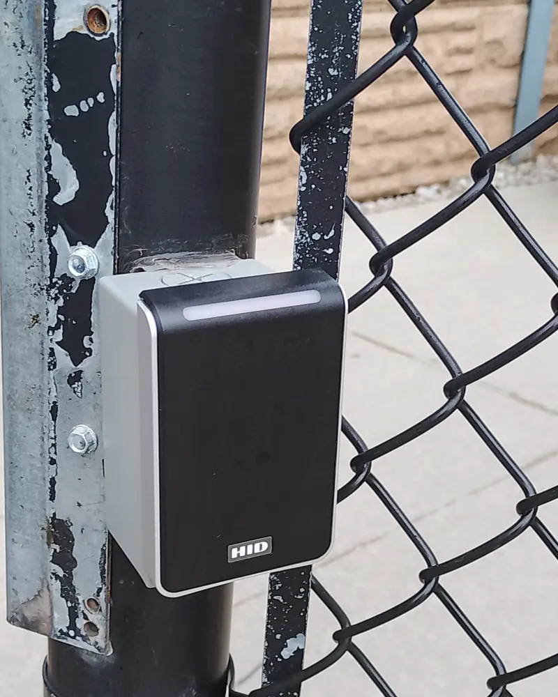 Weatherproof HID Signo smart-card reader mounted on the steel post of a chain-link yard gate in Brampton, ON.